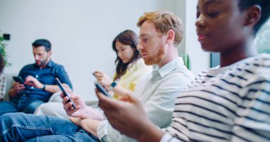 Sıralarını beklerken koltuklarda oturan insanların yan görüntüsü. Akıllı telefonlarda vakit geçirmek. Web taraması ya da kayan sosyal medya. Mobil cihazlar. Sakince bir şey bekliyorum. Teknoloji.