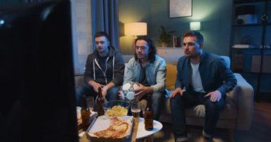 Beyaz tenli en iyi üç erkek, favori futbol takımı için tezahürat yapıyor ve oturma odasında pizza ve bira içerken çok endişeleniyor. Erkekler golü mü kutluyor yoksa maçı mı?.