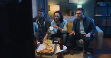 En sevdiği futbol takımı için tezahürat yapan ve gergin bir şekilde oturma odasında pizza ve birayla televizyon karşısında oturan üç beyaz adam. Erkekler golü mü kutluyor yoksa oyunu mu?.