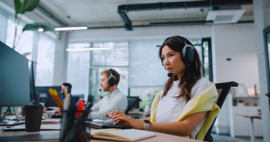 Güzel bir kadın, müşterisine kulaklıkla danışıyor. İş arkadaşları kadınların yanında oturuyor. Çalışkan yöneticiler çevrimiçi hizmet sağlıyorlar. Müşterilerle daha iyi bağlantı kurmak için bilgisayar kullanmak.