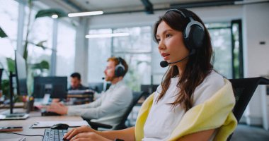 Side view of hardworking operators using headsets while consulting customers from office. Workers sitting at computer and entering information on keyboard. Providing support for clients. clipart