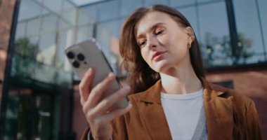 Binanın önünde duran ve tek eliyle akıllı telefonunu kullanan beyaz tatlı bir kız. Ekrana bakıyorum. Mesaja en iyi cevabı düşünüyorum. Cep telefonundan video veya akış izleniyor.