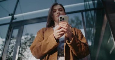 Kamera, modern binanın önünde duran muhteşem beyaz kadına daha da yaklaşıyor. Cep telefonu cihazını kullanarak. Arkadaşlarıyla ya da akrabalarıyla mesajlaşıyorlar. Kameraya bakıp gülümsüyor..