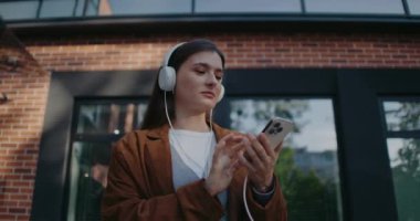 Kafkasyalı mutlu kız dışarıda vakit geçiriyor. Beyaz kulaklık takıp tek parmakla akıllı telefonun ekranına mesaj yazmak. Ne cevap vereceğimi düşünüyorum. Favori albümün tadını çıkarıyorum.