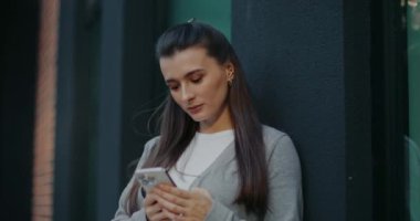 Kamera, kadının etrafında hareket ederken beyaz çekici bir kıza odaklanıyor. Binanın duvarına yaslanan ve akıllı telefonunu kullanan bir kadın. Arkadaşımı bekliyorum. Sosyal medya taranıyor.