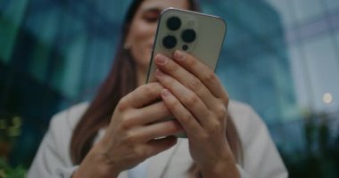 Kamera, birden fazla kameralı beyaz akıllı telefonun arka tarafına odaklanmış. Beyaz bir kadın mesaj girerken iki eliyle mobil cihaz tutuyor. Sosyal medyayı kullanarak. Şehirde akşam.