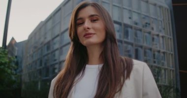 Kameraya yakın duran güzel beyaz kadın. Sırıtırken doğrudan bak. Kahverengi gözlü. Makyaj yapıyor. Bulanık arka planda ışık parlıyor. Şehir merkezinin ortasında..
