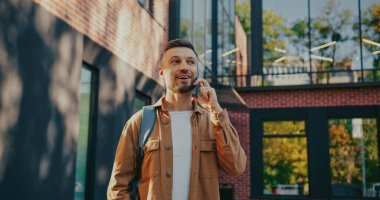 Akıllı telefon tutan ve uzaktan biriyle konuşan çekici, beyaz bir adam. Arka planda modern bina.