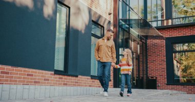 Çekici beyaz bir baba küçük kızıyla konuşuyor. Sarı saçlı çocuk. Okula beraber yürürken ebeveynler çocukla tartışıyor. El ele tutuşmak. Gün için planlardan bahsediyordu..