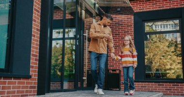 Beyaz adamın küçük kızıyla konuştuğu ön kamera görüntüsü. Gözlüklü ve sırt çantalı çocuk babasının yanında yürüyor. Ailelere okulda aktif bir gün geçirdiklerini söylemek. El hareketleriyle betimleme.