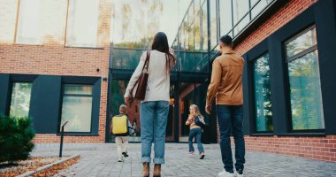 Kafkasyalı karı ve kocanın çocuklarıyla birlikte okula gidişinin görüntüsü. Çocuklar binaya doğru koşarken ebeveynler girişte durur. Dışarıda sonbahar havası.