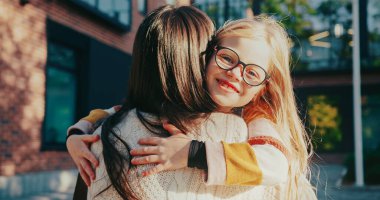 Kamera, annesine sarılan beyaz tatlı bir kıza odaklanıyor. Çocuk sevinçle gülümserken kameraya bakıyor. Gözlüklü ve kalın kazaklı. Olumlu bir an. Aile toplantısı. Parlak güneş ışığı.