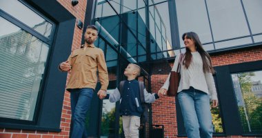 Oğlan mavi bir ceket giyiyor ve bir sırt çantası taşıyor. Bu da okula ya da okula gittiklerini gösteriyor. Ayar parlak ve güneşli, camlarda yansıyan ağaçlar var..