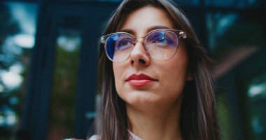 Çekici beyaz kadın kameraya bakıp gülümsemeden önce gökyüzüne bakıyor. Daha iyi görebilmek için büyük yuvarlak gözlükler takıyordu. Portre konsepti. Müdür öğle arasında dışarıda vakit geçiriyor..