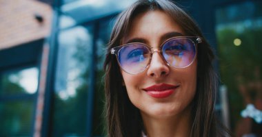 Doğrudan kameraya bakıyorum. Yüzünde sıcak bir gülümseme var. Arka plandaki uzun pencerelerde görünen ağaçlar.