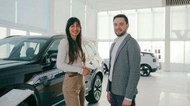 İnsanlar araç alımı hakkında önemli kararlar verirken konuşuyor. Karı koca bir şey tartışıyorlar. Galeride yeni bir araba almak. Kameraya bakmadan önce gülüyorum..