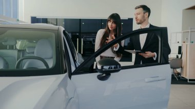 Beyaz tenli çekici bir menajerin yanında duran başarılı bir kadının kamera görüntüsü. Adam yeni ciple ilgili her şeyi anlatıyor. Müşteri için kapıyı açıyorum. Yeni özellikler gösteriliyor.