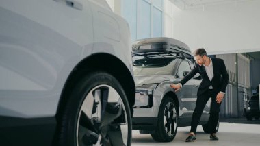 Modern SUV 'un ön kanadıyla sürtünen siyah takım elbiseli yakışıklı beyaz erkek manzarası. Ön kapıyı açmadan ve sürücü koltuğuna oturmadan önce çok güzel bir şekli vardı..