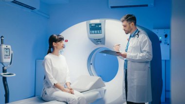 Beyaz kadın odaklı erkek doktor görüntüleme ekipmanlarının yanında dururken panoya gözlemler yazıyor..