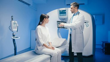 Klinik ortamda, MRI taramalarını inceleyen beyaz bir hasta. Nörolojik sonuçları tartışan ve danışma sürecinde içgörü sunan ayakta duran bir doktor.