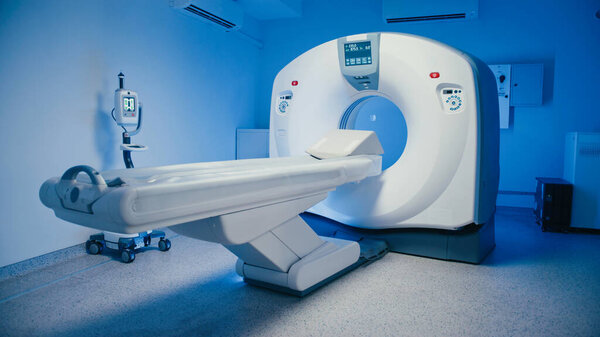 Empty CT scanner room showing diagnostic machine with extended patient table ready for next procedure. Bright display glowing on device while scanning station remains unused and perfectly prepared.