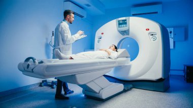 Hasta tarama yatağında dinlenirken gülümseyen yakışıklı erkek doktor. Tomografi işlemleri başlamadan önce kadın dinlenirken arkadaşça sohbete dalıyoruz..
