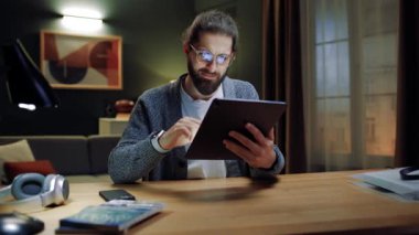 Genç adam evde tek başına oturup, elinde dijital tabletle e-randevu hizmetlerinden keyif alıyor, internette sörf yapıyor, internetten alışveriş yapıyor, sosyal medya uygulamaları kullanıyor. Modern aygıt kullanımı kavramı