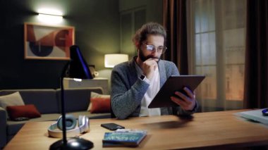 Genç adam evde tek başına oturup, elinde dijital tablet tutarak akşamları e-randevu hizmetlerinin tadını çıkarıyor. Bilgi arıyor, mesaj yazıyor, sosyal ağda uzaktan iletişim kuruyor, alışveriş yapıyor..