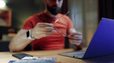 Oturma odasında masada oturan bir erkek. İş adamı yeni projeler yaratıyor. Uzaktan çalışan bir erkek. Serbest çalışmak için dizüstü bilgisayar kullanan bir adam. Ciddi bir adam laptop ekranına bakıyor. Gözlük takan adam.