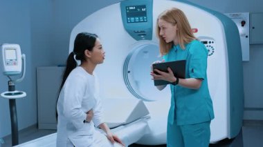 Hasta, tomografi masasında otururken mide ağrısından şikayetçi. Çağdaş klinikte biyopsi röntgeni muayenesi. Tıbbi tesiste MRI makinesi ve çağdaş ekipman.