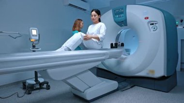 Hasta, manyetik rezonans tomografi prosedüründen önce tomografi odasında yatarken doktordan tavsiye alıyor. Nörobiyolog doktor tomografi görüntüleme yapıyor..