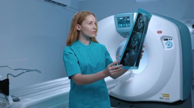 MRI kabinesinde mavi üniformalı bir doktor. MRI taraması. Doktor MRI görüntüsünü inceliyor. MRI kapsüllü modern donanımlı dolap. CT tarayıcılı klinik dolabı. İnceleme için makine.