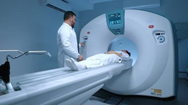 Radyologun bilgisayarlı tomografi odasında hastası var. Hasta ve işlem prosedürünün yanında duran kendine güvenen bir doktor. Tıp çalışanı nörolog, MRI cihazına düğme takıyor..
