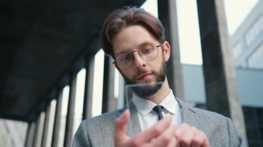 Beyaz sakallı, gözlüklü, takım elbiseli ve kravatlı, şeffaf ekranlı fütüristik akıllı telefon kullanan bir adam. Gelecek kavramı. Hologram. Dokunma aygıtı