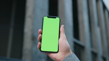 Bulanık arka planda akıllı telefon model ekranı kullanan bir adam. Erkeğin elini dikey pozisyonda tut yeşil renkli akıllı telefon ve şehir caddesinde dokunmatik ekran kullan..