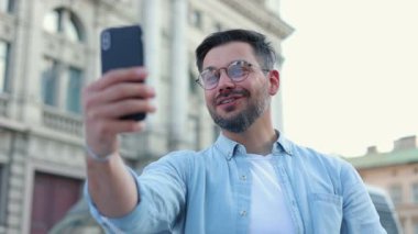 Gözlüklü, elinde akıllı telefon olan ve ailesine Skype 'ta eski şehir caddesini gösteren Kafkasyalı turist portresi. Turist konsepti. Seyahat ediyorum. Gözlem