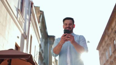 Beyaz bir erkeğin elinde akıllı telefon tutarken görüntüsü. Gün batımında sokakta cihaz kullanan genç bir adamın portresi. E- postaları kontrol eden adam, konsepti kullanan aygıt