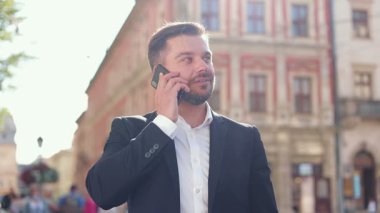 Resmi takım elbiseli kendine güvenen genç yönetici telefonda konuşurken. Yaşam tarzı. İşe giderken cep telefonuyla konuşan gülümseyen beyaz erkek girişimci. Başarı kavramı