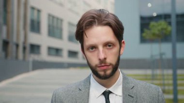 Yavaş çekimde genç bir iş adamının portresi. Takım elbiseli ciddi bir erkek büro merkezinin yakınındaki kameraya bakıyor. Takım elbiseli sakallı bir erkek..