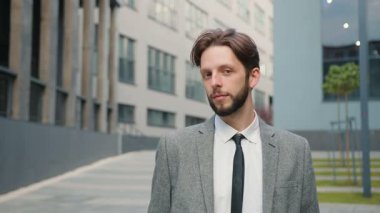 Ofis merkezinin yanında duran takım elbiseli genç bir erkek üzerinde harika bir portre. Kameraya gülümseyen akıllı takım elbiseli sakallı bir erkek. İşte mutlu ofis çalışanı.