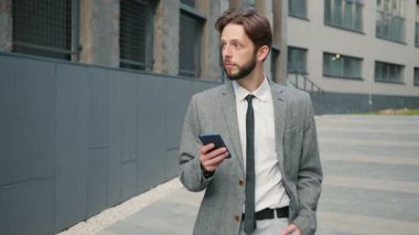 İş merkezinin yakınındaki caddede yürüyen sakallı beyaz bir adamın portresi. Adam yürüyor ve zamanı kontrol ediyor. Takım elbiseli sakallı bir erkek..