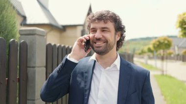 Sakallı ve kıvırcık saçlı bir adamın portresi sokakta telefonuyla konuşuyor. İş adamı dışarıda telefonla konuşuyor. Akıllı telefondan konuşan başarılı bir adam. Ofis çalışanı caddedeki telefonu arıyor..