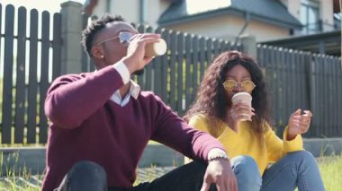 Güzel Afro-Amerikan erkek ve kadın sinemada yan yana oturup kahve içiyorlar. Çift sıcaklığın ve güneş ışığının tadını çıkarıyor. Güneş gözlüklü insanlar.