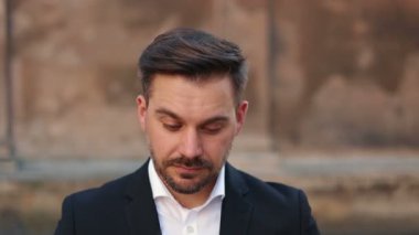 Yakın çekimde, gözlük takan, sakallı, beyaz, yakışıklı genç bir adamın sinematik portresi. Erkek ciddi görünüyor ve dişleriyle gülümsüyor. Akıllı takım elbiseli adam kameraya bakıyor..