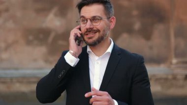 Yakın plan, sakallı, yakışıklı, beyaz bir adamın sinematik portresi. Gözlüklü adam telefonda konuşuyor. Takım elbiseli adam etrafa bakıyor. Elleriyle hareket eden bir erkek..