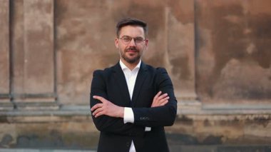 Ön tarafta, sakallı ve ellerini çaprazlayan yakışıklı beyaz bir adamın sinematik portresi var. Erkek ciddi görünüyor. Akıllı takım elbiseli adam kameraya bakıyor ve gülümsüyor..