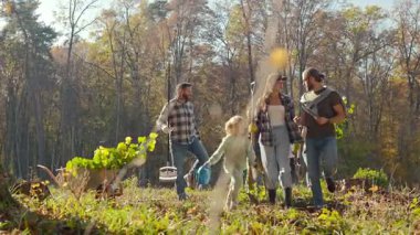 Çocuklu beyaz insanlar ağaçların filizleriyle ormanda yürüyorlar. Ağaç dikme konsepti. Açık havada. Güneşli bir sonbahar günü. Erkekler ve kadınlar çocuklarla birlikte parka gidecekler. Gönüllüler.