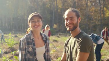 Portrait of young Caucasian joyful happy couple of environmental volunteers talking and smiling to camera in park on sunny day. Planting seedlings of trees concept. Outside. Environmental.