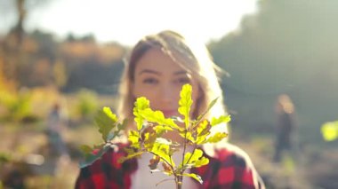 Güzel beyaz kadın gönüllü ve bahçıvanın ellerinde saksıda filizlenen ağaç fidanına yakın durun. Bahçede güneşli bir gün. Çekici kadın ve bitki portresi. Ekosistem kavramı.