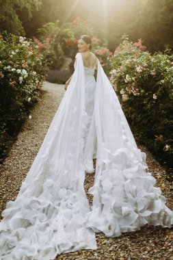 Akan beyaz elbisesiyle güzel bir gelin büyüleyici çiçeklerle dolu romantik bir bahçede zarifçe yürüyor.